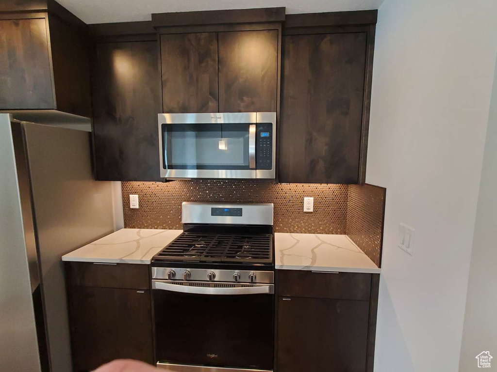 Kitchen with appliances with stainless steel finishes, tasteful backsplash, dark brown cabinets, and modern cabinets