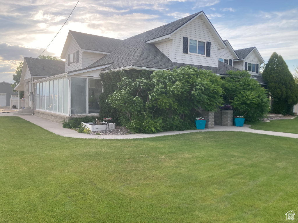 Back of house featuring roof with shingles, a sunroom, and a lawn