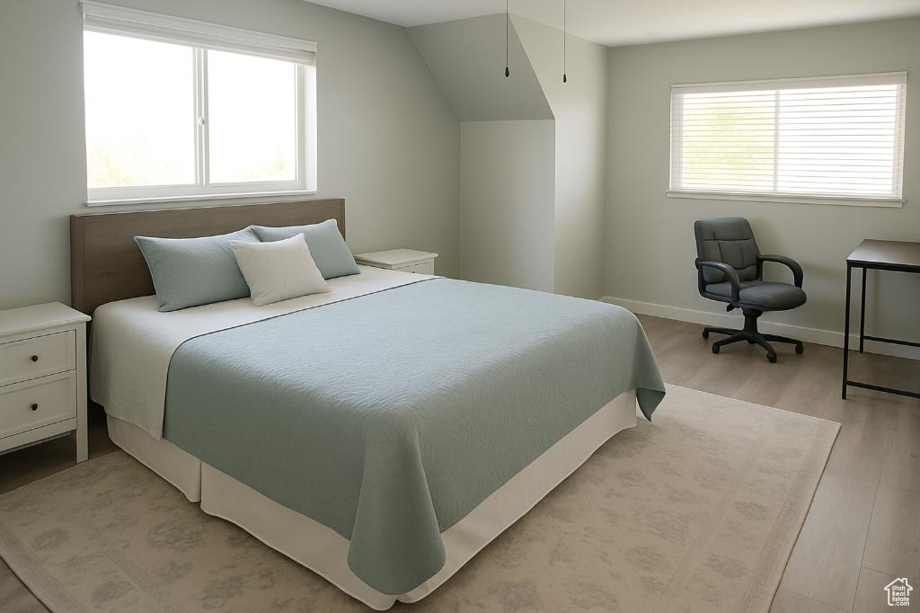 Bedroom featuring light wood-type flooring, multiple windows, baseboards, and vaulted ceiling