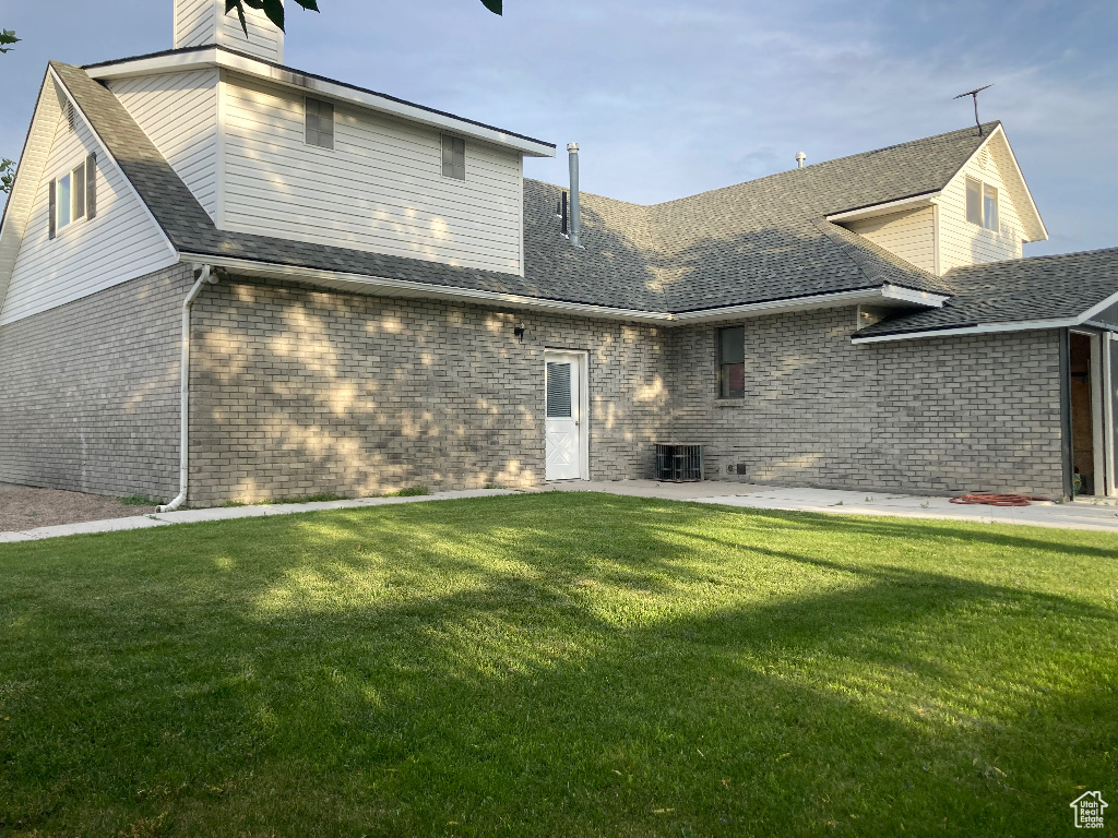 Rear view of property with a yard, brick siding, a chimney, a shingled roof, and a patio area