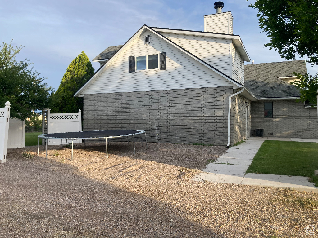 View of side of property with a trampoline, a chimney, and brick siding