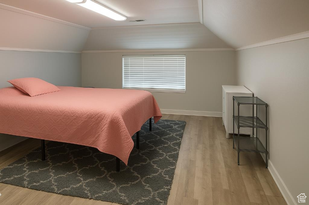 Bedroom with vaulted ceiling, wood finished floors, and baseboards