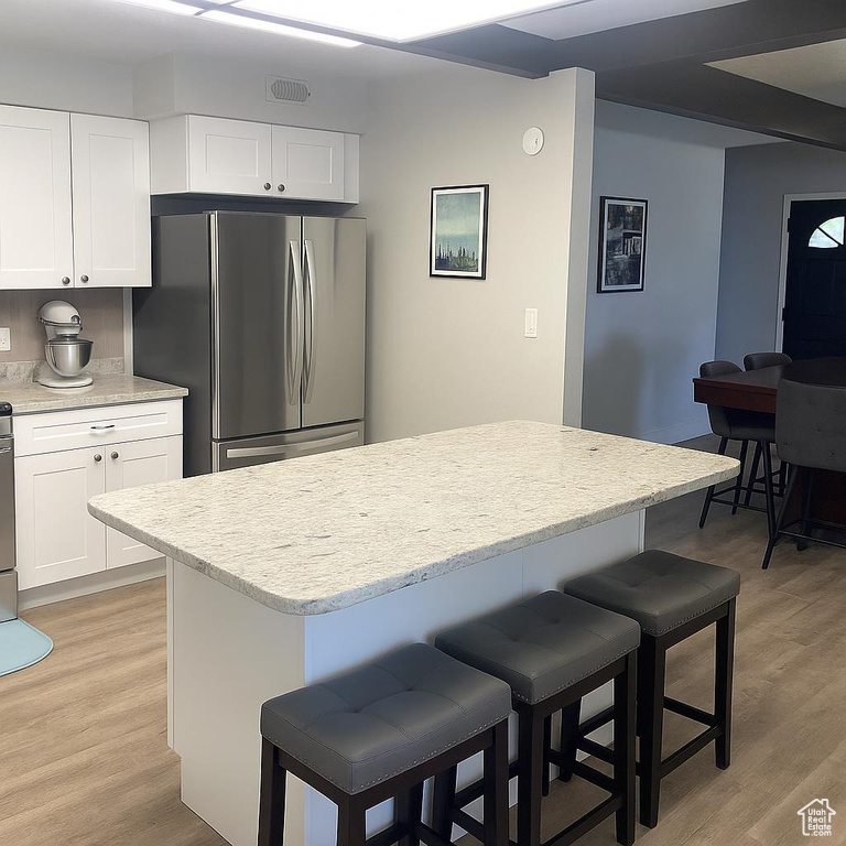 Kitchen featuring freestanding refrigerator, a kitchen breakfast bar, light wood finished floors, and white cabinetry