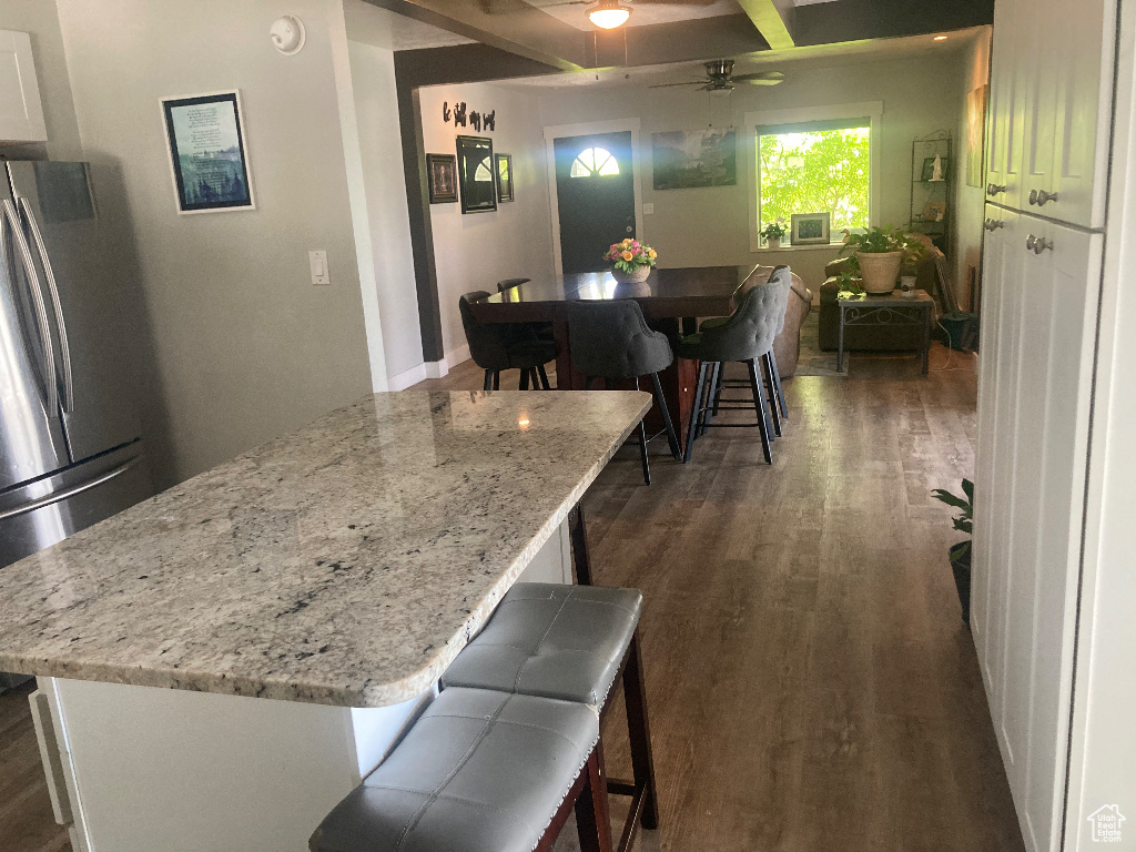 Kitchen with dark wood-type flooring, freestanding refrigerator, a ceiling fan, and light stone counters
