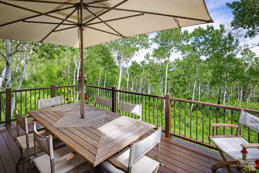 Wooden terrace featuring outdoor dining space and view of wooded area