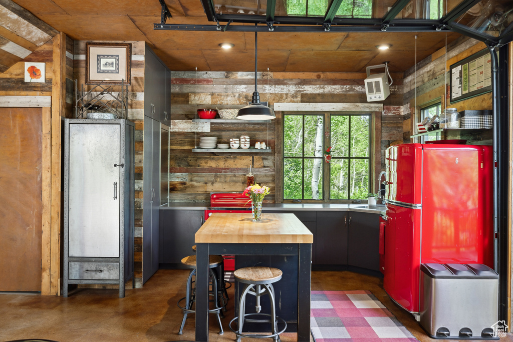 Kitchen with butcher block counters, freestanding refrigerator, wood walls, a sink, and concrete flooring