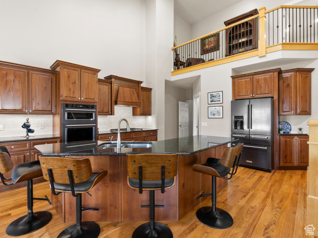 Kitchen with high end refrigerator, a towering ceiling, light wood-type flooring, a sink, and a kitchen breakfast bar