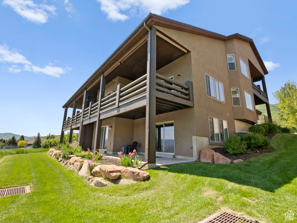 Rear view of property with stucco siding, a lawn, and a balcony