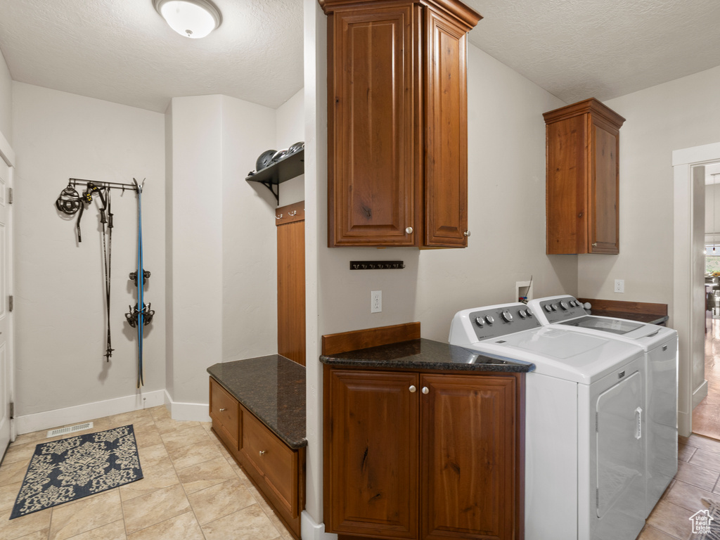 Laundry area with cabinet space, washer and dryer, baseboards, a textured ceiling, and light tile patterned floors