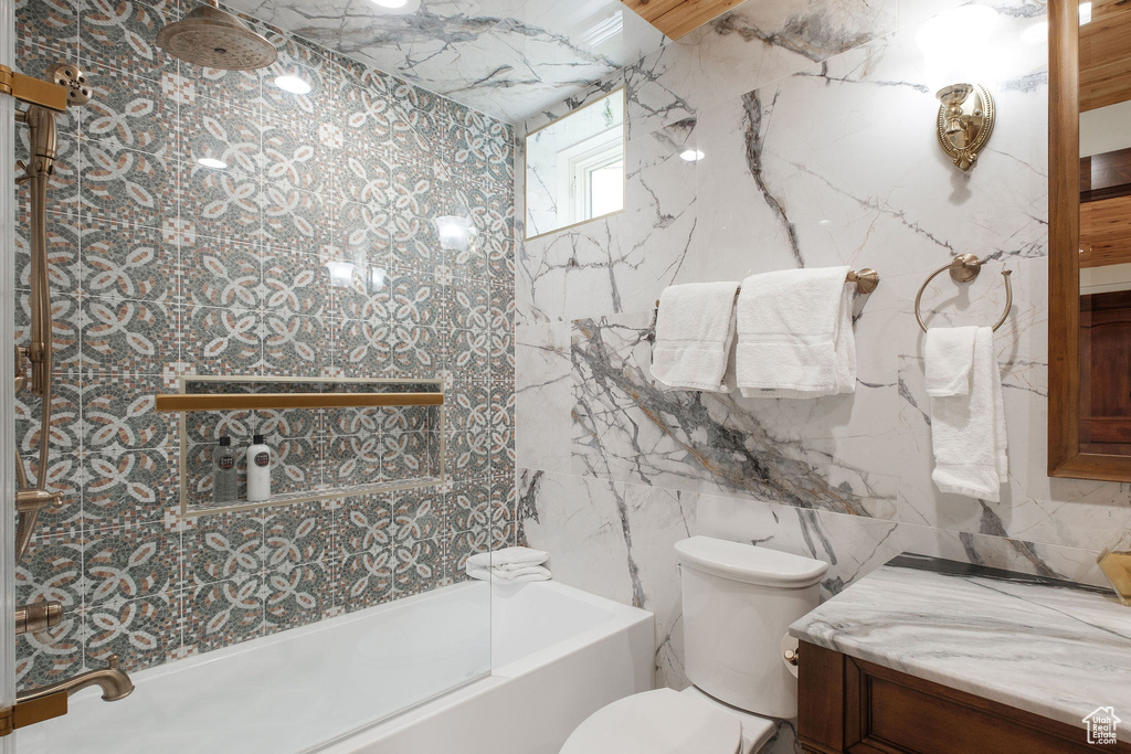 Bathroom with tile walls, toilet, vanity, and shower / bathtub combination