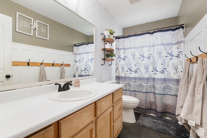 Bathroom with toilet, vanity, tile patterned flooring, wainscoting, and curtained shower
