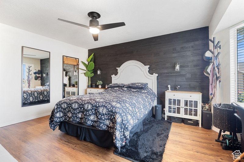 Bedroom featuring wood finished floors, baseboards, an accent wall, and wooden walls