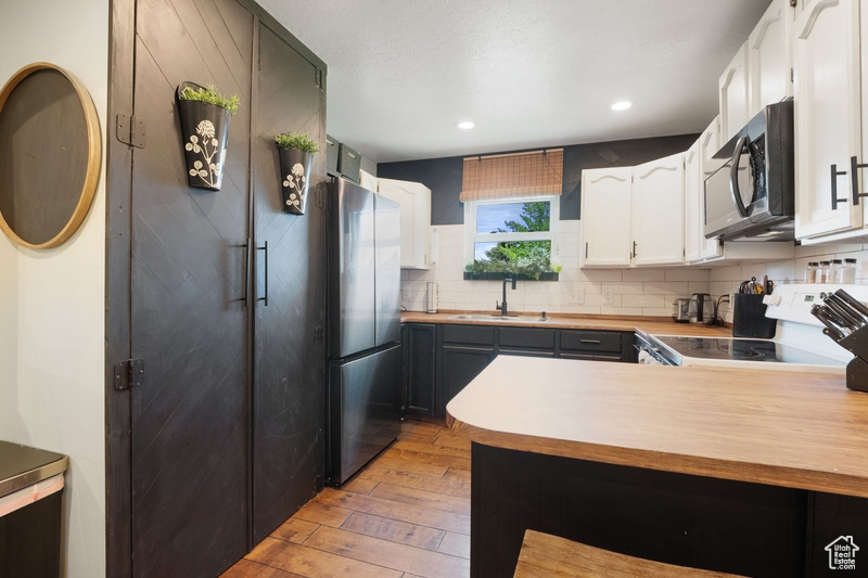 Kitchen featuring freestanding refrigerator, range, light wood-type flooring, a sink, and decorative backsplash