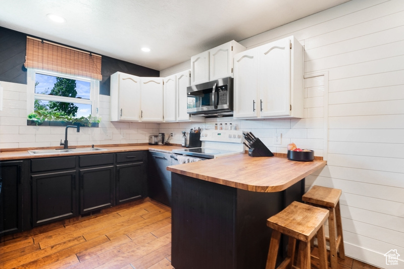 Kitchen featuring stainless steel microwave, white range with electric cooktop, a sink, white cabinets, and light wood-type flooring