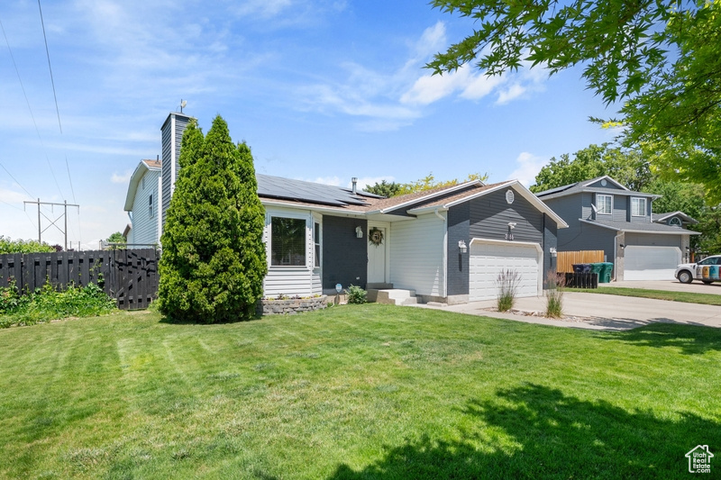 View of front facade with an attached garage, roof mounted solar panels, concrete driveway, and a chimney