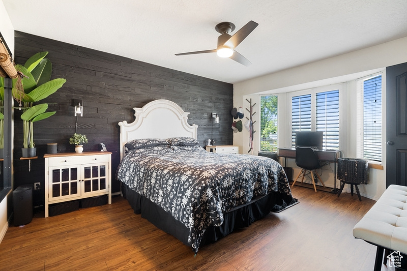 Bedroom featuring a desk, an accent wall, wood walls, wood finished floors, and a ceiling fan