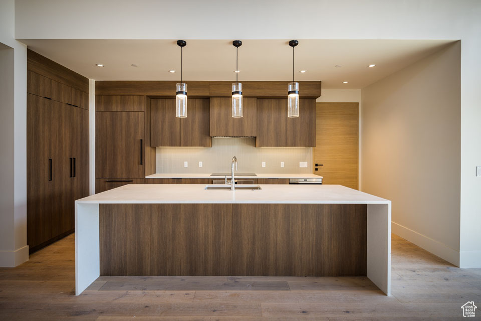 Kitchen with modern cabinets, a sink, a large island, tasteful backsplash, and baseboards