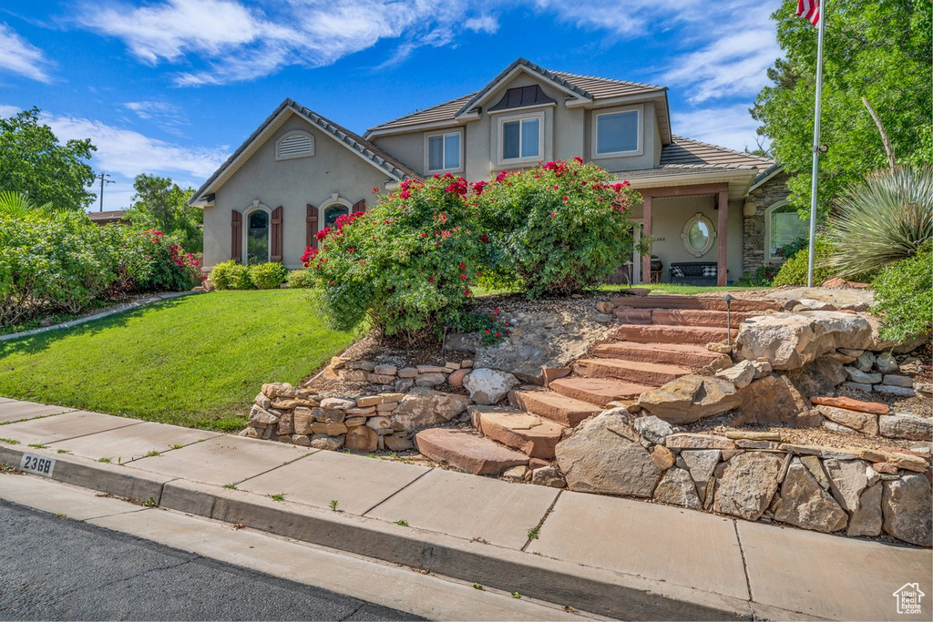 View of front of house featuring stucco siding, a front yard, and a tile roof