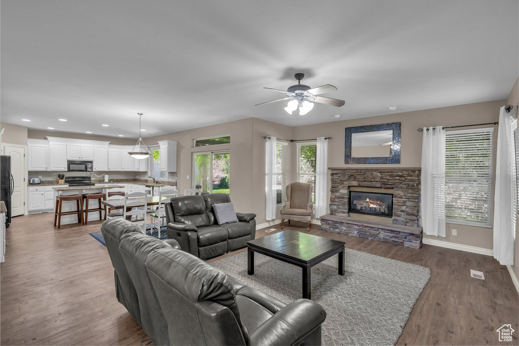 Living room with a ceiling fan, a stone fireplace, light wood finished floors, and recessed lighting