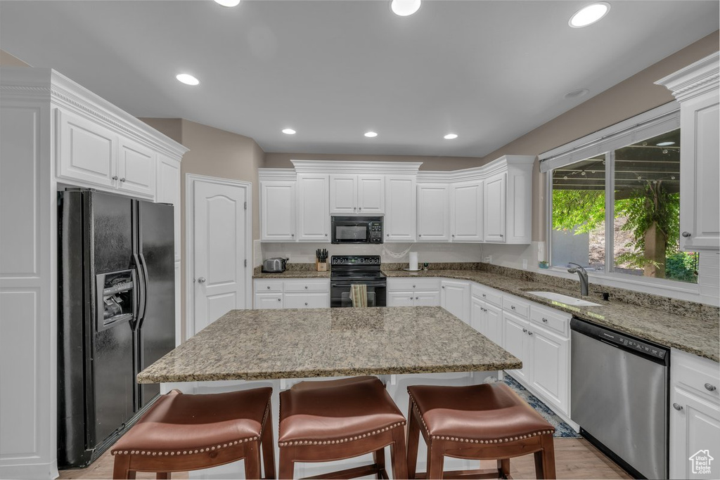 Kitchen featuring black appliances, a center island, white cabinets, a kitchen bar, and recessed lighting