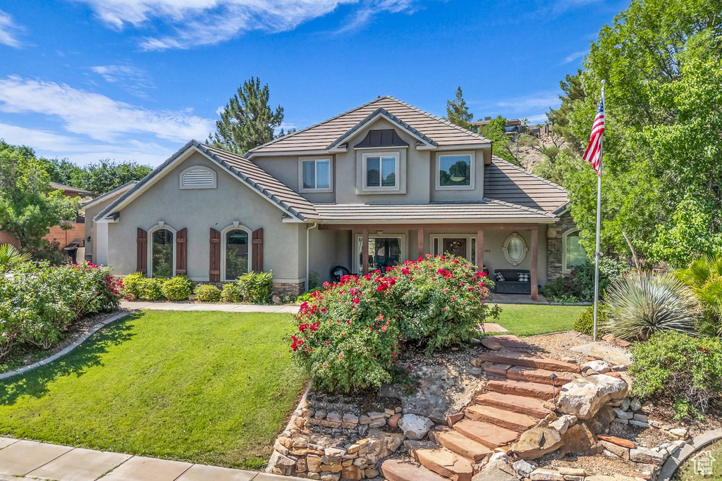 View of front of house featuring stucco siding, a tile roof, a front yard, and a porch