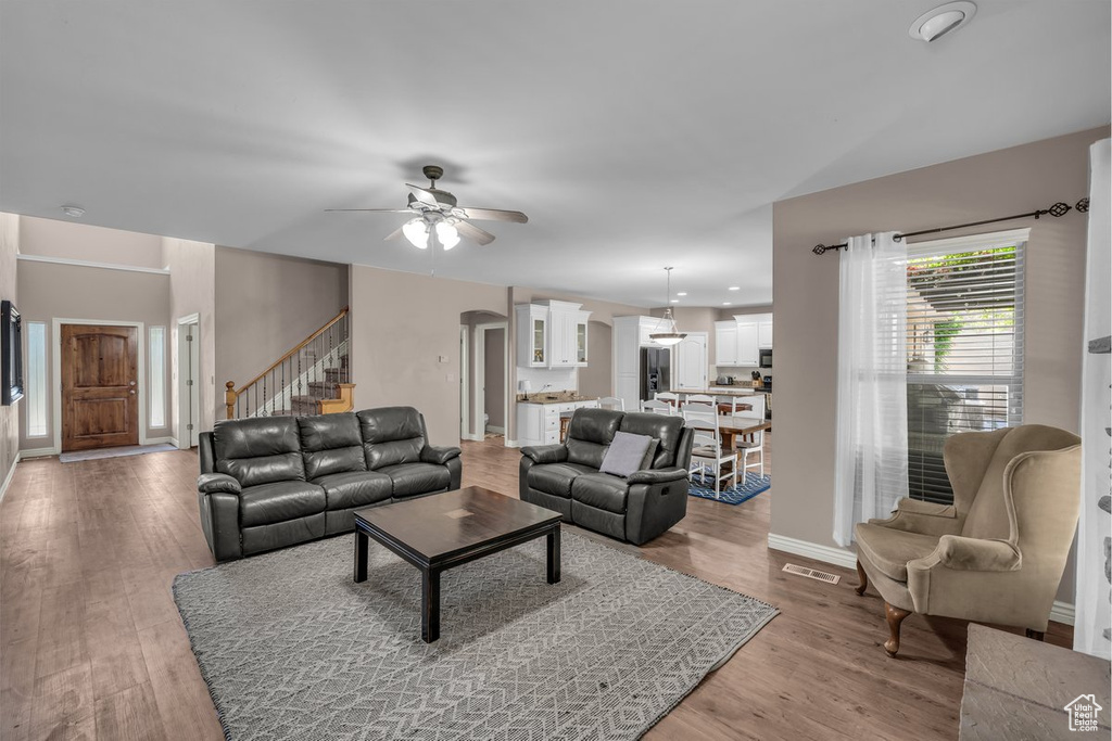 Living area with ceiling fan, stairway, light wood-style floors, and arched walkways