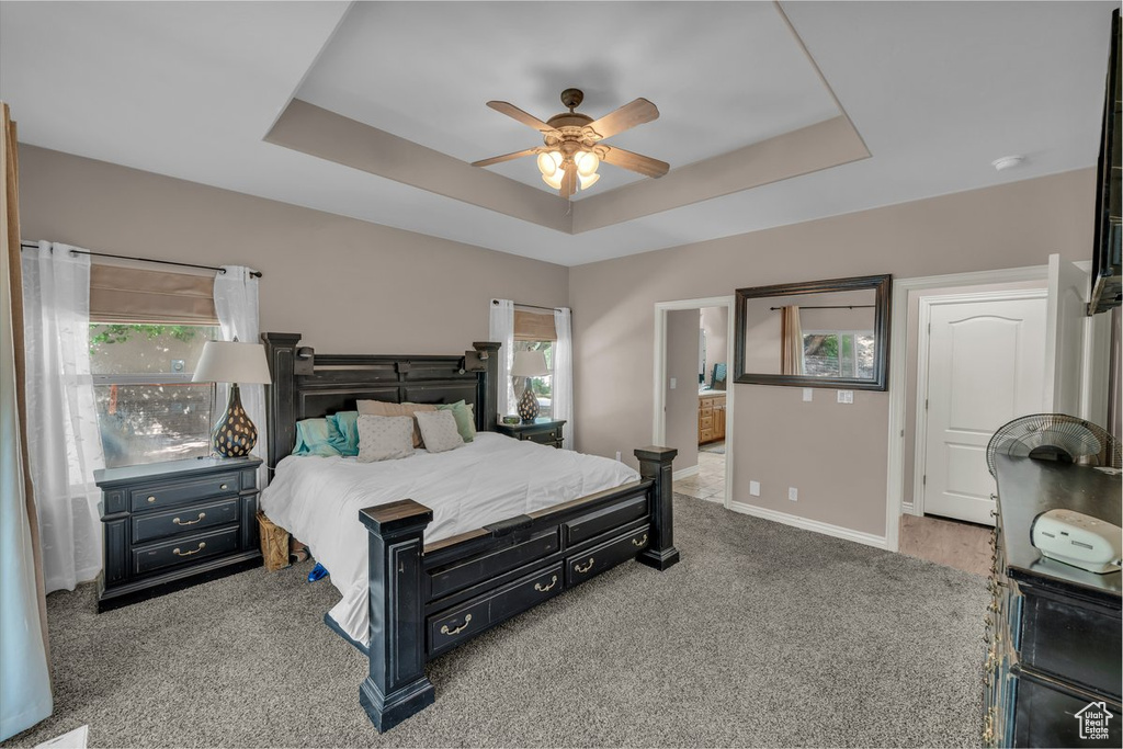 Carpeted bedroom with a tray ceiling, a ceiling fan, and ensuite bath