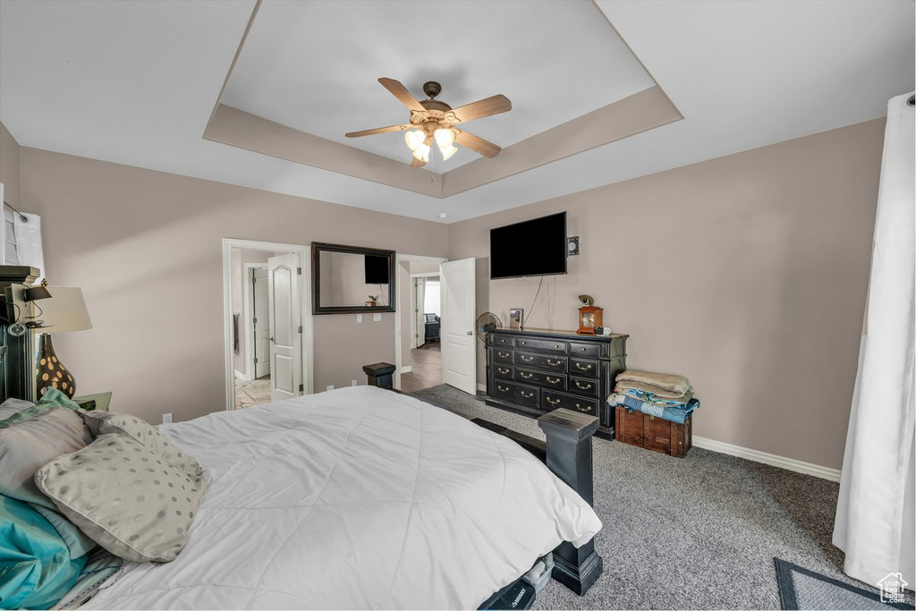 Carpeted bedroom featuring a tray ceiling and a ceiling fan