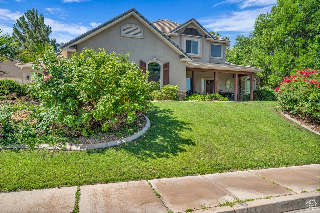 View of front of home featuring stucco siding, a front yard, and covered porch