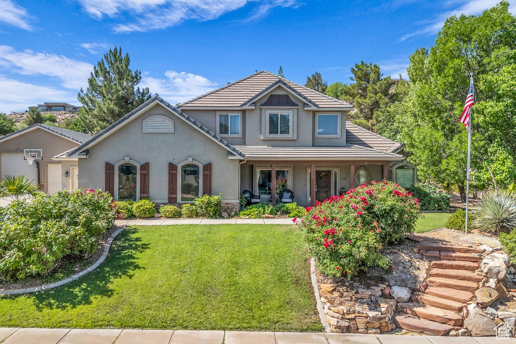 View of front of home with stucco siding, a front lawn, a tile roof, and covered porch