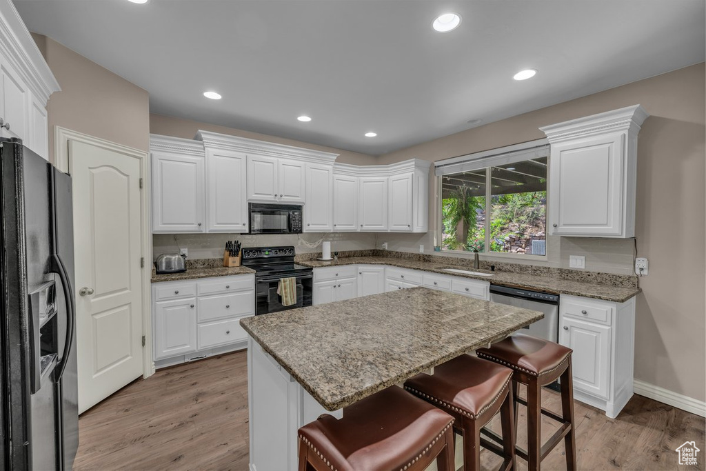 Kitchen featuring black appliances, a breakfast bar, light wood finished floors, white cabinets, and recessed lighting