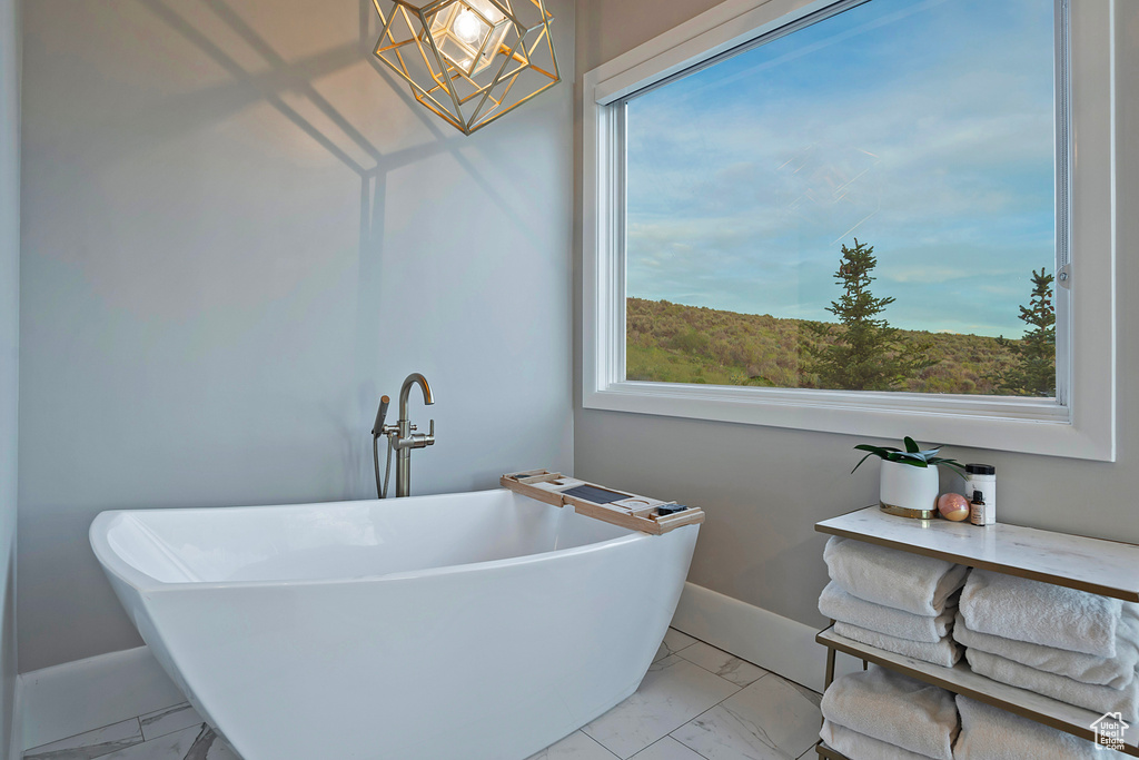 Full bathroom with marble look tiles, healthy amount of natural light, a soaking tub, and baseboards