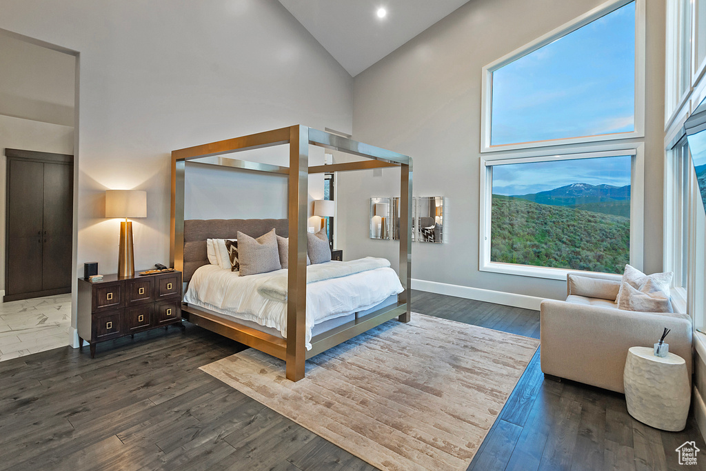 Bedroom with high vaulted ceiling, dark wood-type flooring, multiple windows, baseboards, and recessed lighting