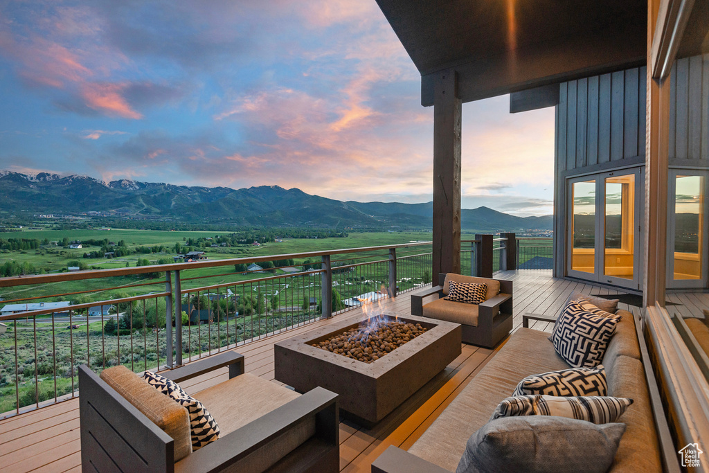 Deck at dusk featuring an outdoor living space with a fire pit, a mountain view, and a view of countryside