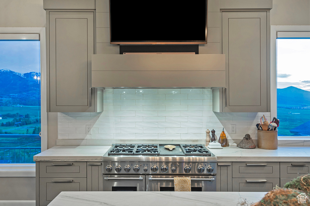 Kitchen featuring gray cabinetry, range with two ovens, decorative backsplash, light stone counters, and extractor fan