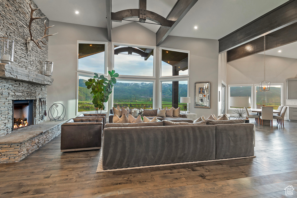 Living area featuring high vaulted ceiling, a stone fireplace, dark wood-type flooring, beamed ceiling, and a ceiling fan