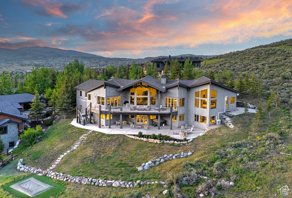 Back of property at dusk with a patio area, a chimney, a deck with mountain view, and dirt driveway