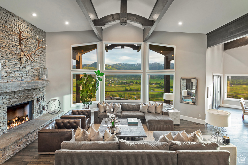 Living area featuring a high ceiling, dark wood finished floors, ceiling fan, a stone fireplace, and baseboards