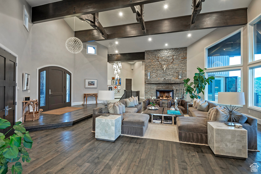 Living area with high vaulted ceiling, beam ceiling, dark wood-type flooring, arched walkways, and a stone fireplace
