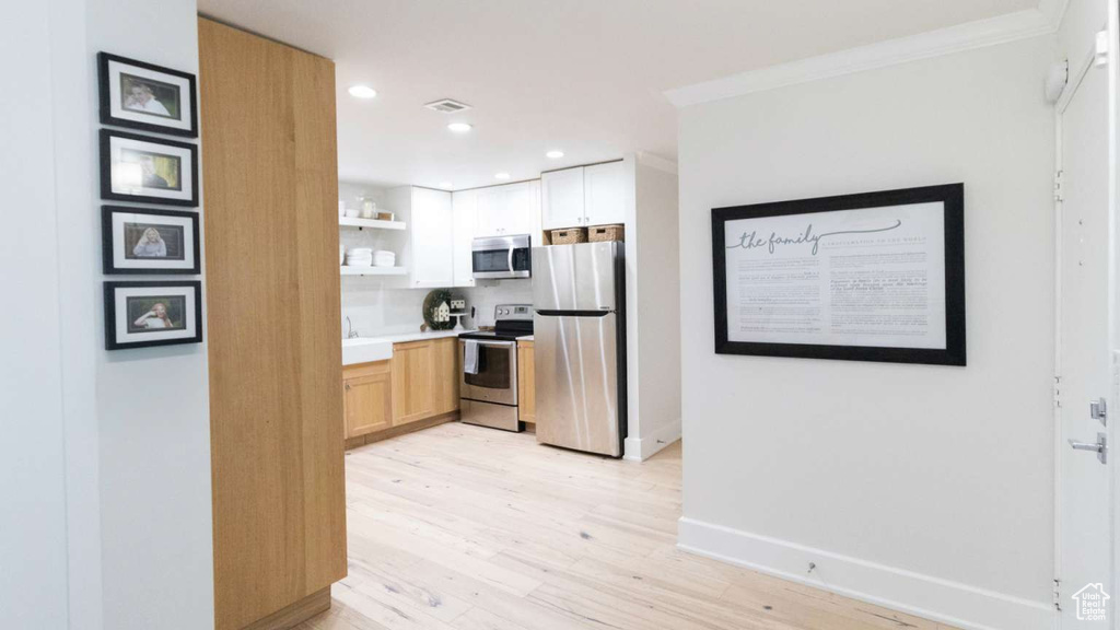 Kitchen featuring stainless steel appliances, open shelves, light wood-type flooring, crown molding, and recessed lighting