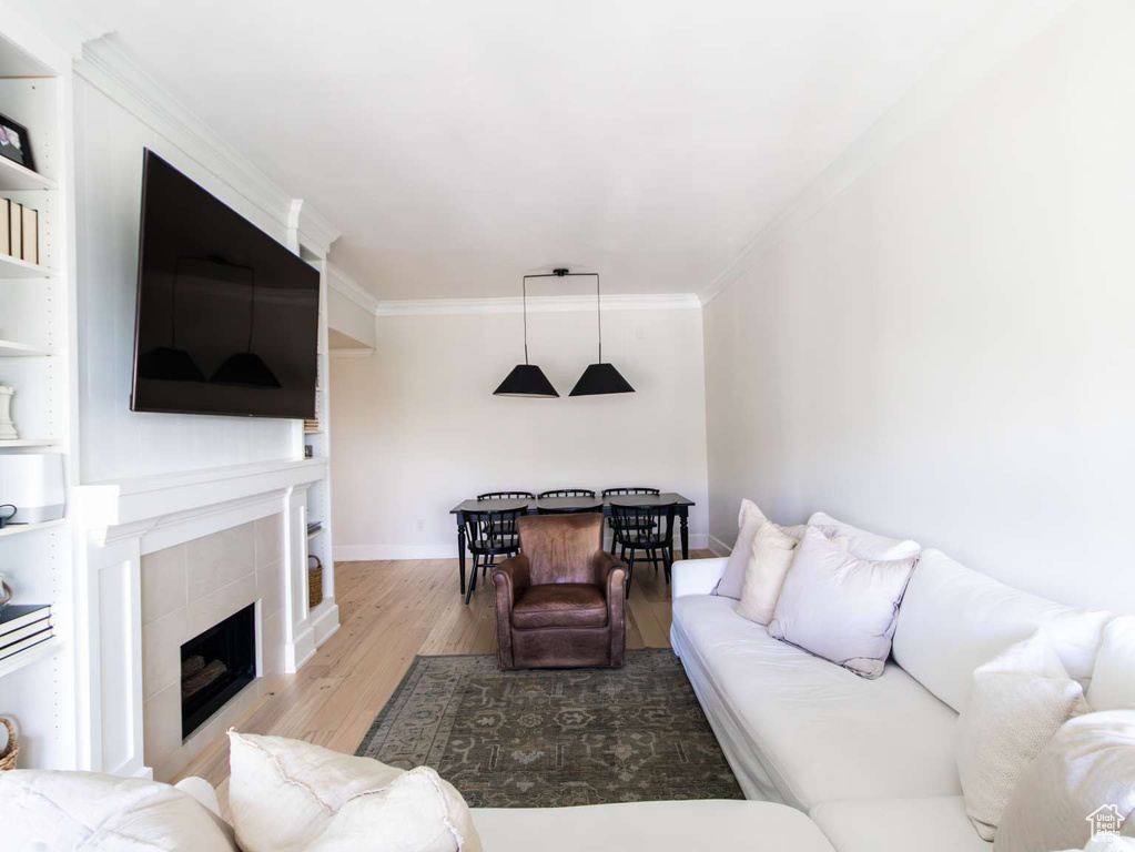 Living room featuring wood finished floors, crown molding, a tiled fireplace, and baseboards