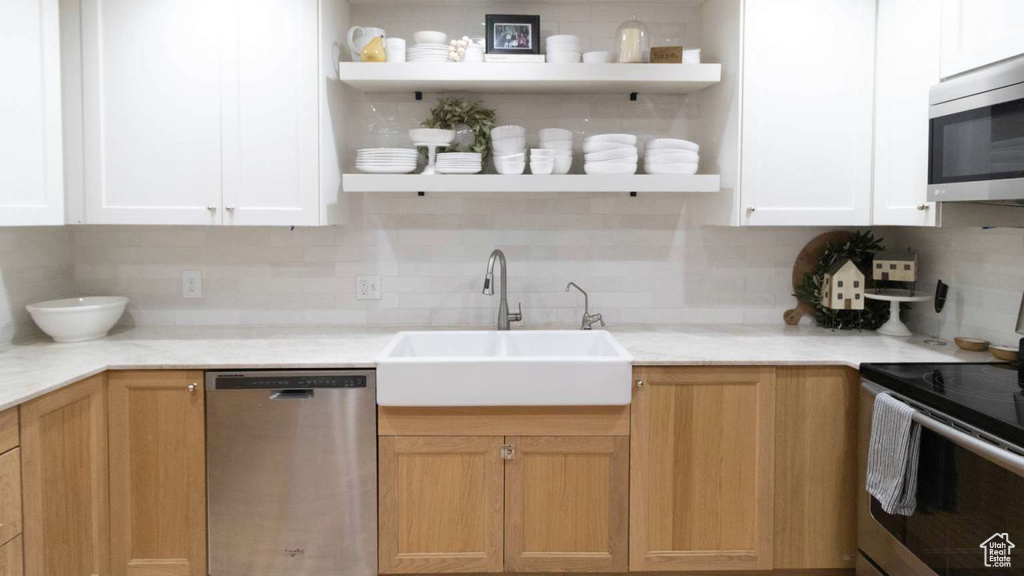 Kitchen featuring stainless steel appliances, open shelves, a sink, tasteful backsplash, and light countertops