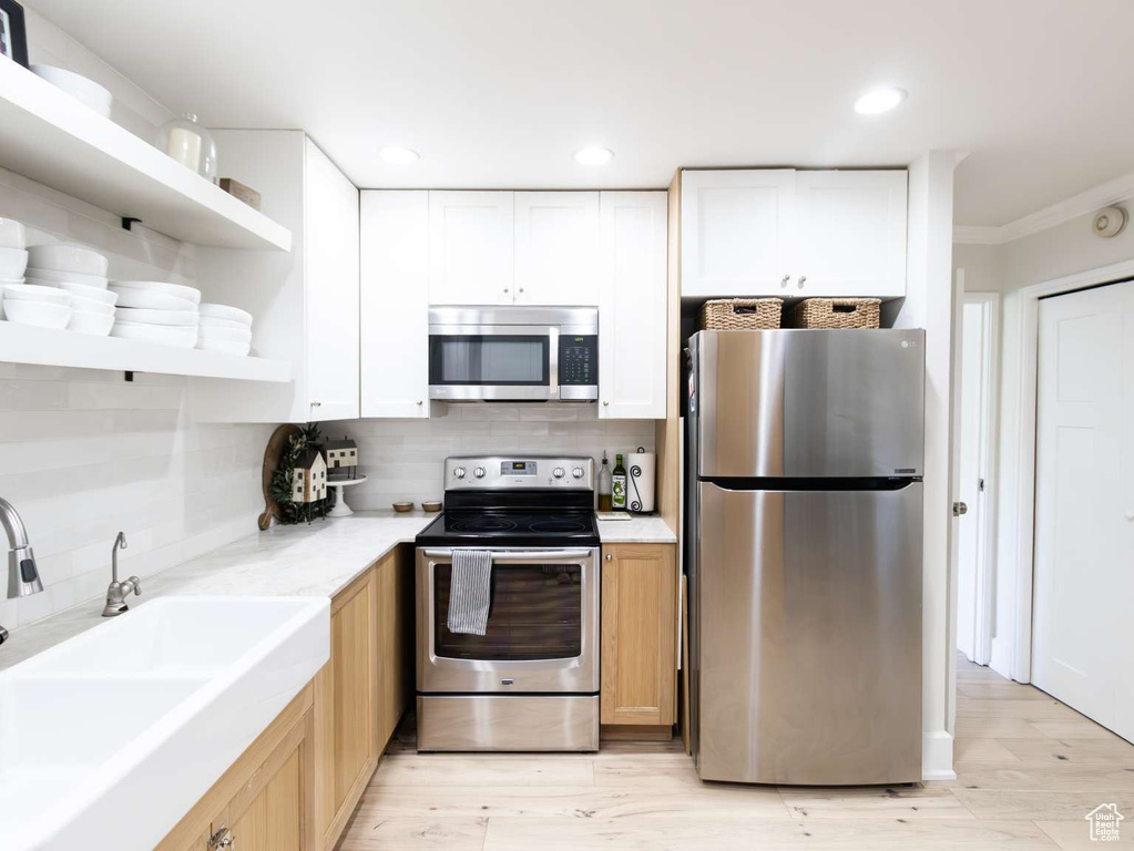 Kitchen with stainless steel appliances, a sink, open shelves, backsplash, and white cabinets