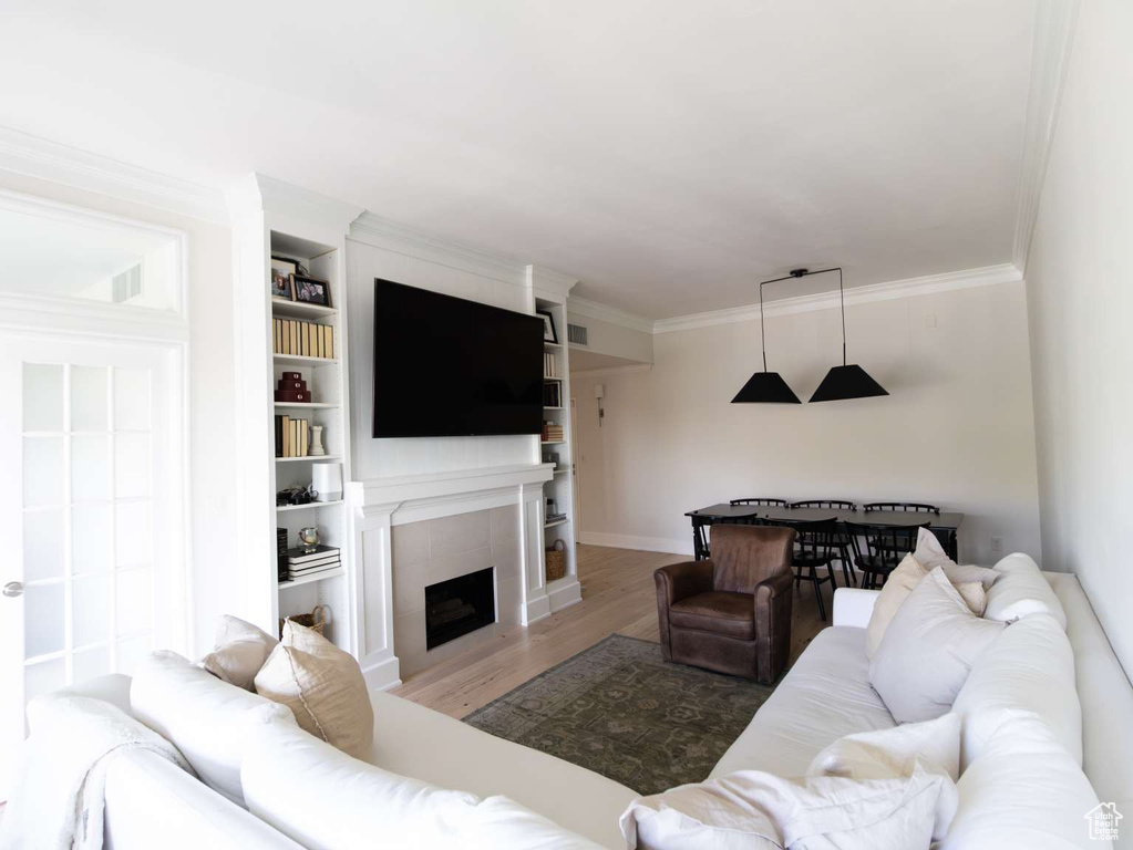 Living room featuring wood finished floors, crown molding, a tiled fireplace, built in shelves, and baseboards