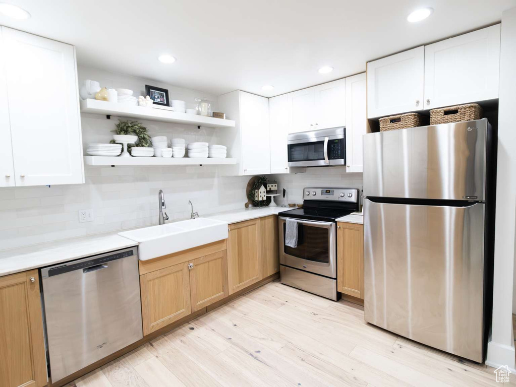 Kitchen featuring stainless steel appliances, a sink, open shelves, light countertops, and tasteful backsplash