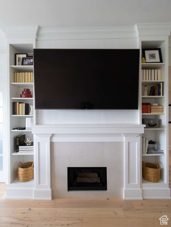 Detailed view of a tiled fireplace, wood finished floors, and ornamental molding