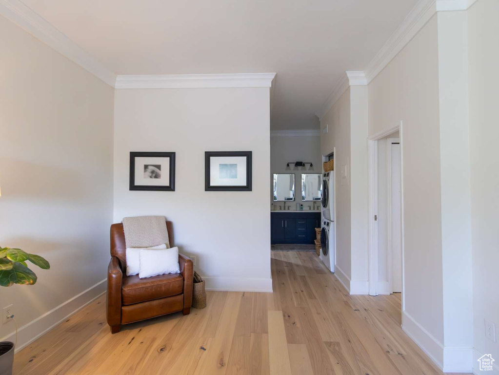 Sitting room featuring wood finished floors, stacked washing machine and dryer, crown molding, and baseboards