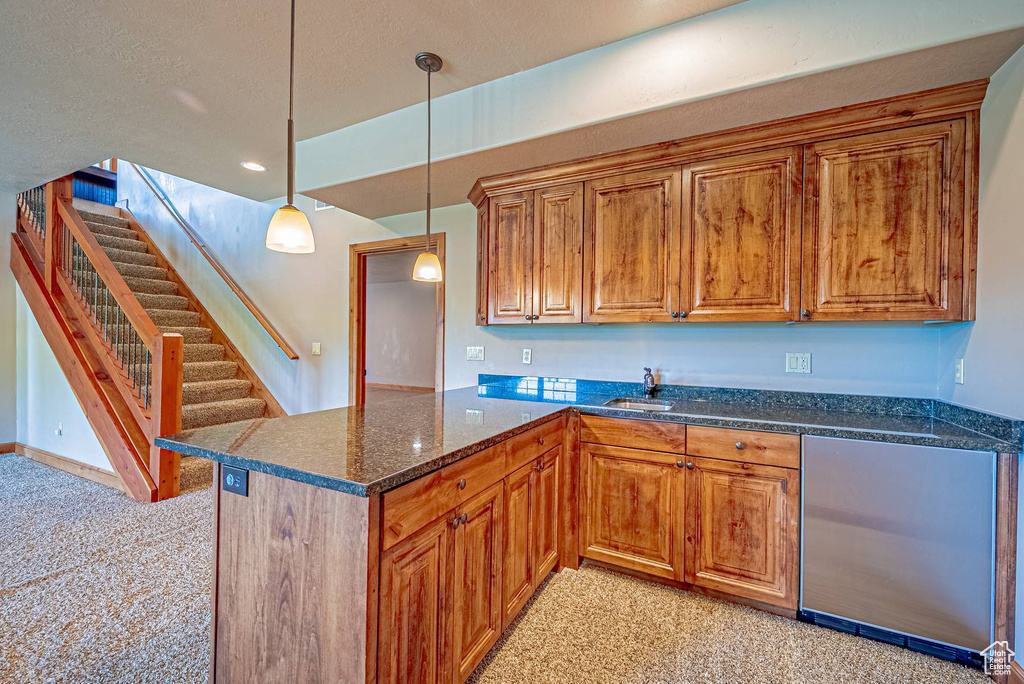 Kitchen featuring light colored carpet, a sink, brown cabinets, pendant lighting, and a textured ceiling