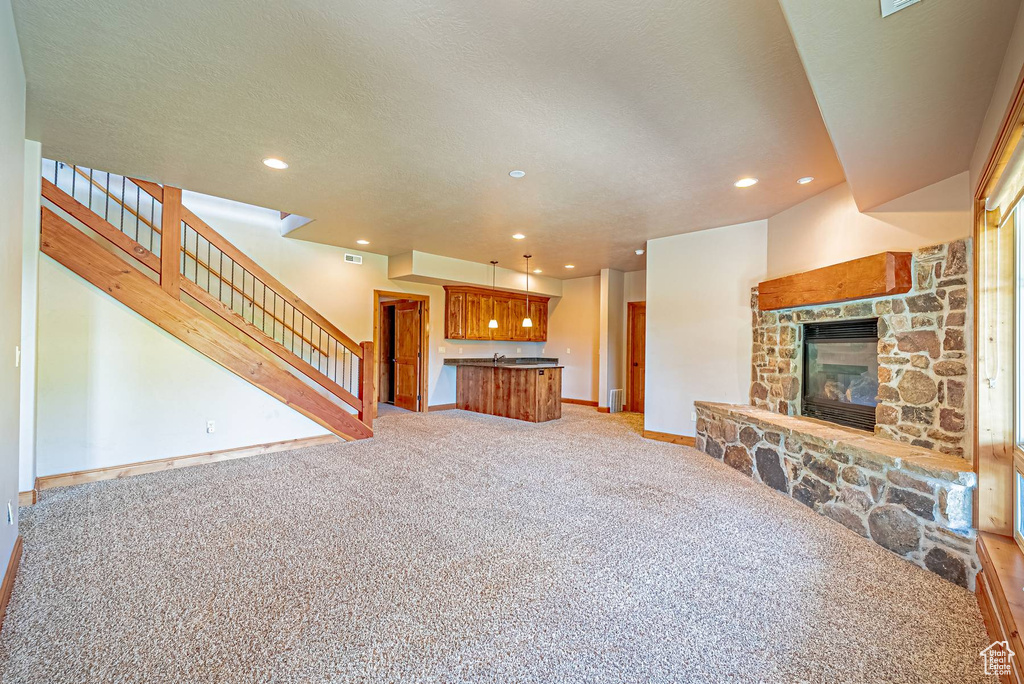 Unfurnished living room with light carpet, recessed lighting, stairway, baseboards, and a stone fireplace
