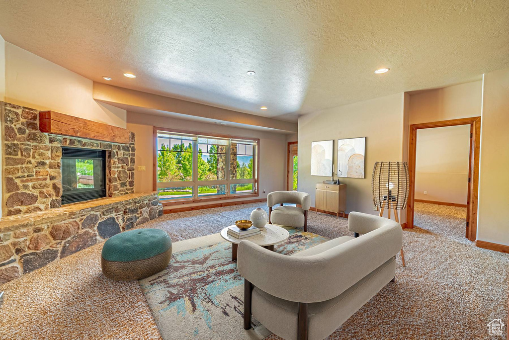 Carpeted living room with a textured ceiling, recessed lighting, a stone fireplace, and baseboards